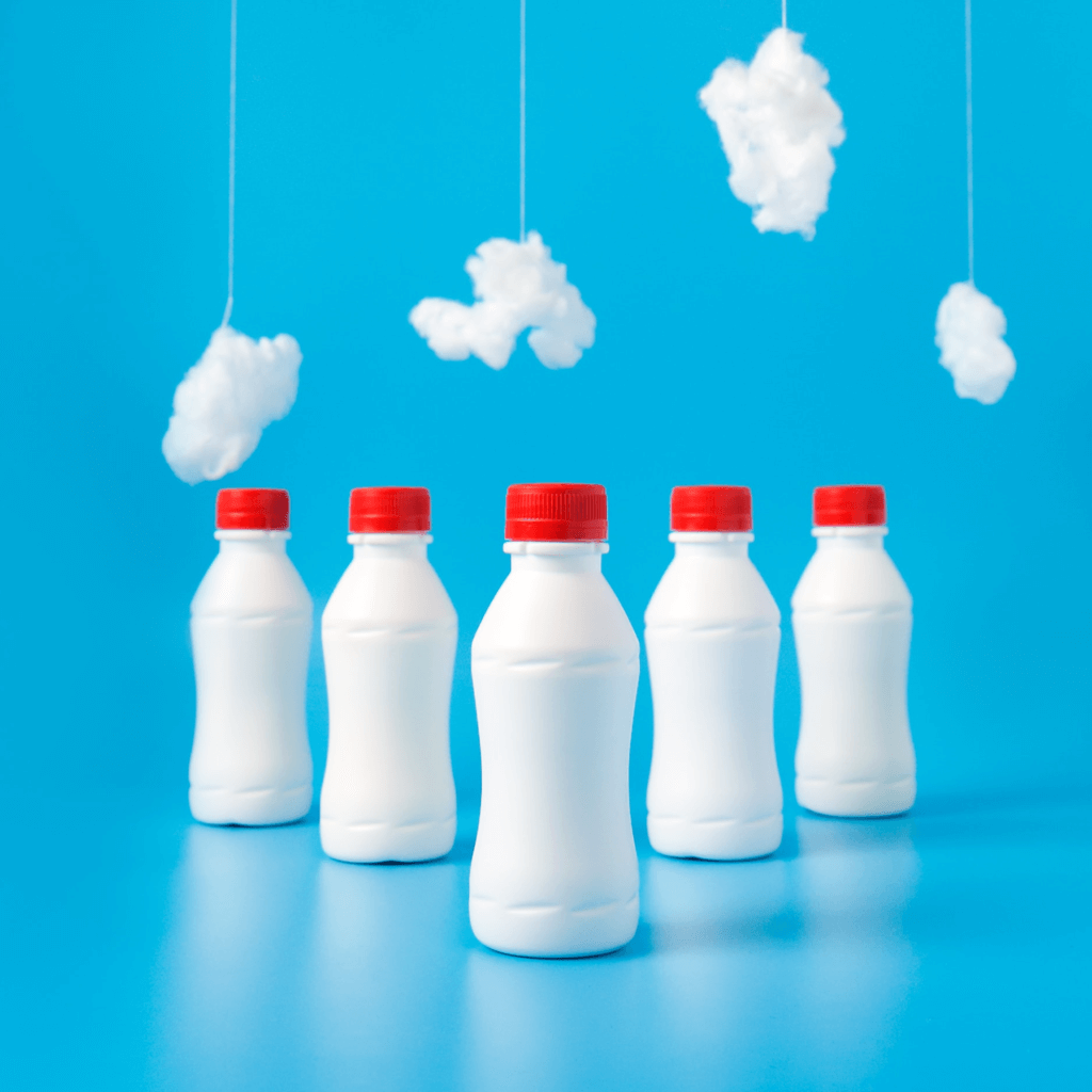 Botellas de plástico alineadas sobre un fondo azul con nubes de algodón